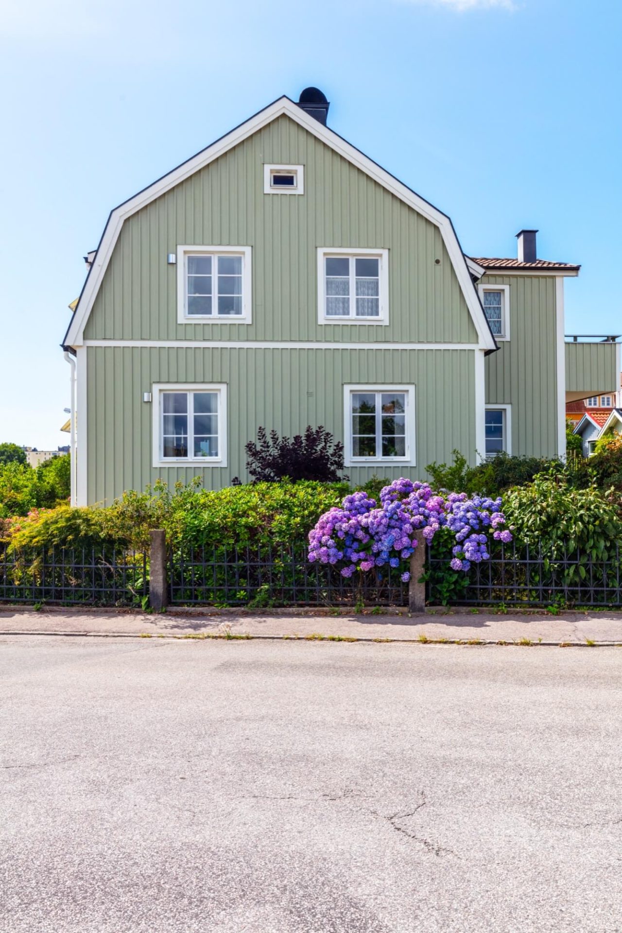 Grönt trähus prytt med vita fasaddetaljer och en trädgård där lila hortensior står i full blom