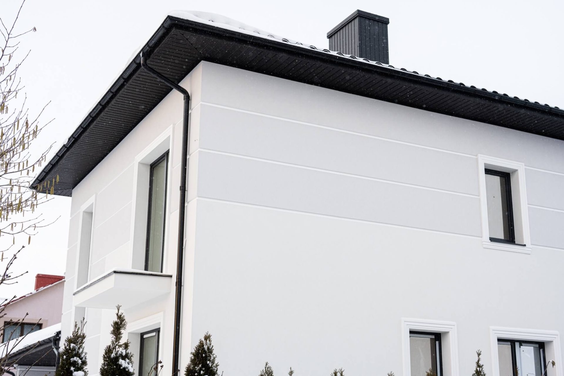 En vit villa i modern stil, kompletterad med ett svart tak och snöiga detaljer under vinterperioden